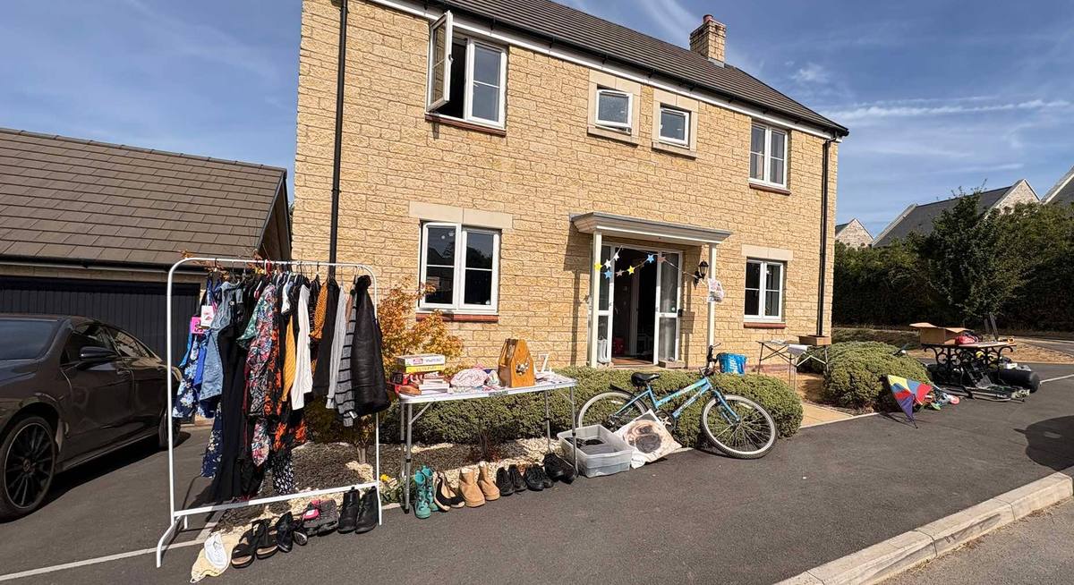 A driveway sale on the jumble trail: a clothes rail, a table of books and shoes lined along the kerb outside a village house
