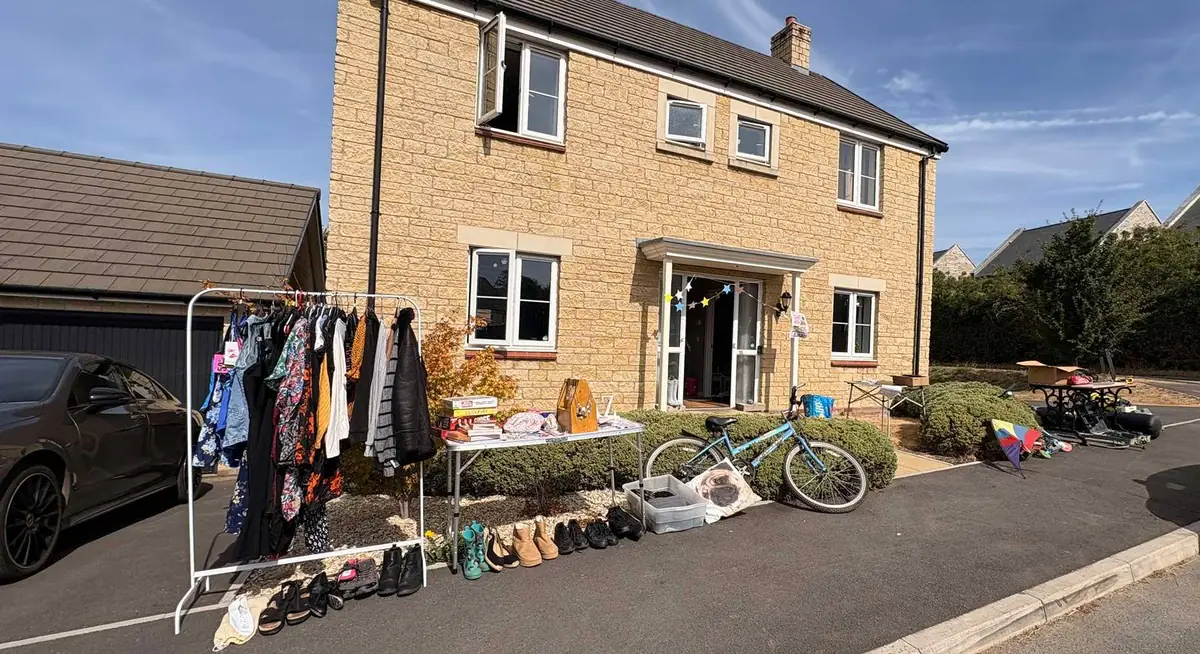 A driveway sale on the jumble trail: a clothes rail, a table of books and shoes lined along the kerb outside a village house